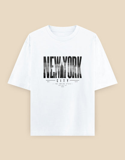White oversized t-shirt featuring a bold New York City typography graphic with a monochrome skyline integrated into the lettering.
