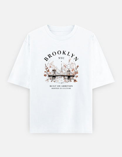 White oversized t-shirt featuring a vintage Brooklyn Bridge illustration with floral accents and classic "Brooklyn NYC" typography printed on the front.jpg