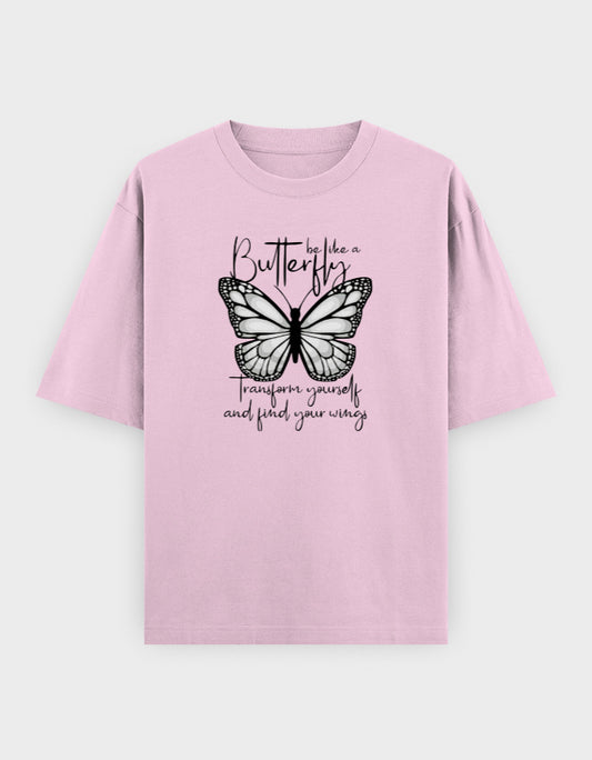 Pastel pink oversized t-shirt featuring a black butterfly illustration with the inspirational quote "Be Like a Butterfly – Transform Yourself and Find Your Wings" printed on the front.