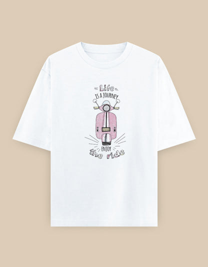 White oversized t-shirt featuring a vintage pink scooter illustration with the inspirational quote "Life Is A Journey – Enjoy The Ride" printed on the front.