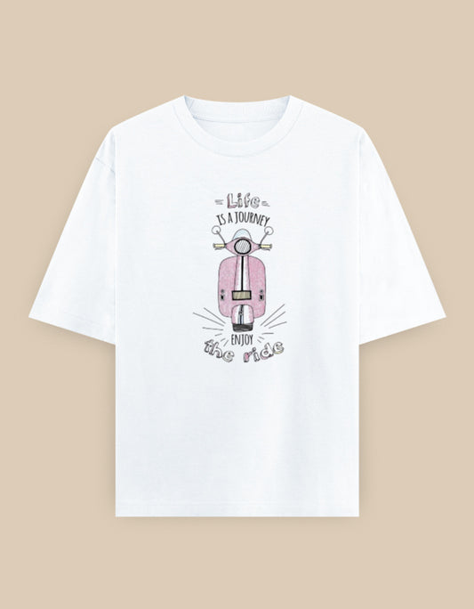 White oversized t-shirt featuring a vintage pink scooter illustration with the inspirational quote "Life Is A Journey – Enjoy The Ride" printed on the front.